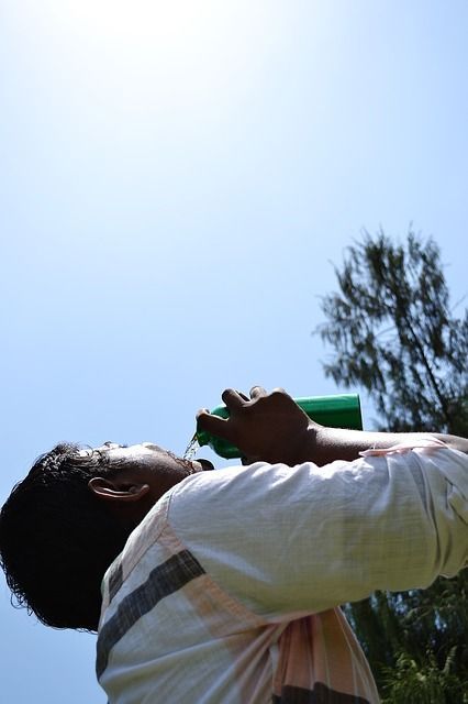 Mann trinkt Wasser aus einer Flasche und blickt gen Himmel