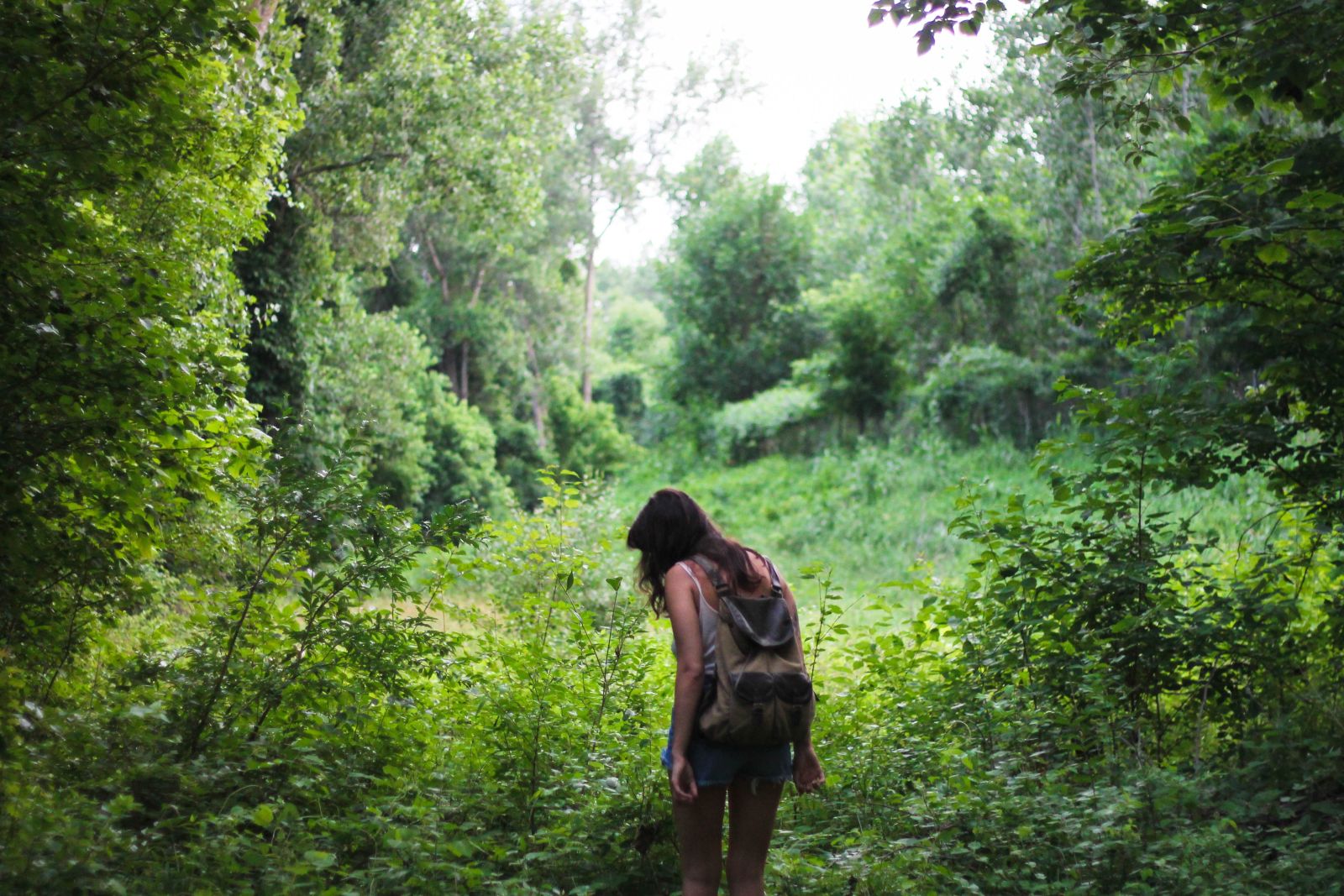 Junge Frau mitten im Wald an einer Lichtung schaut zu Boden