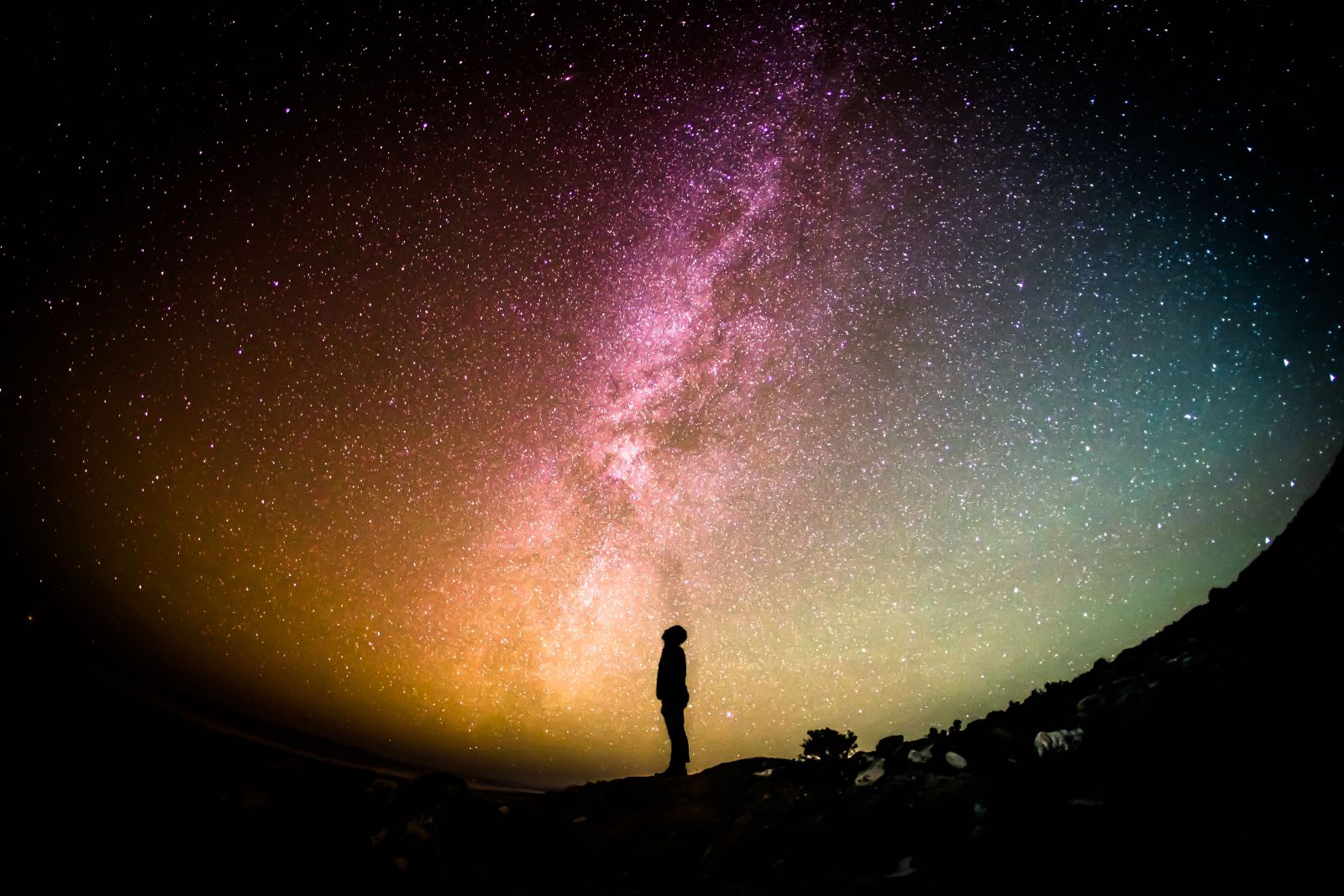 Ein Mann steht unter den Sternen und blickt gehn bunten Nachthimmel. Man sieht die Milchstraße. Das Ganze wurde mit einem Fishey aufgenommen.
