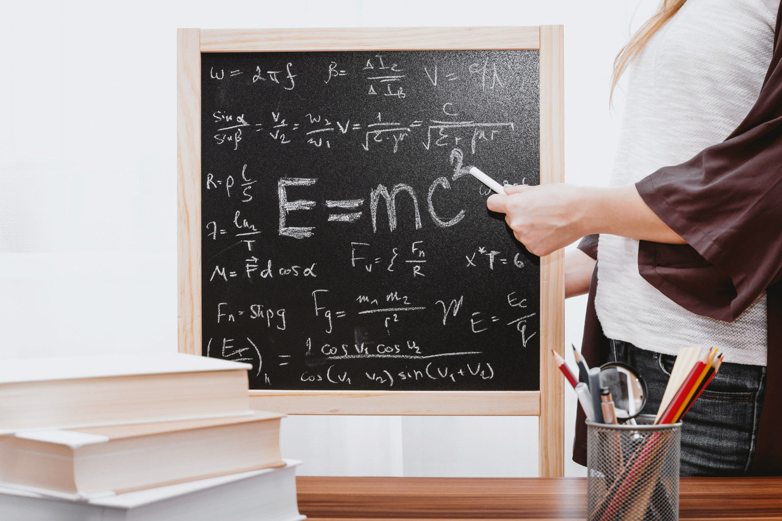 Einsteins Formal E-mc² auf einer kleinen Tafel stehend und eine junge Frau rechts daneben stehend die mit einer Kreide darauf zeigt